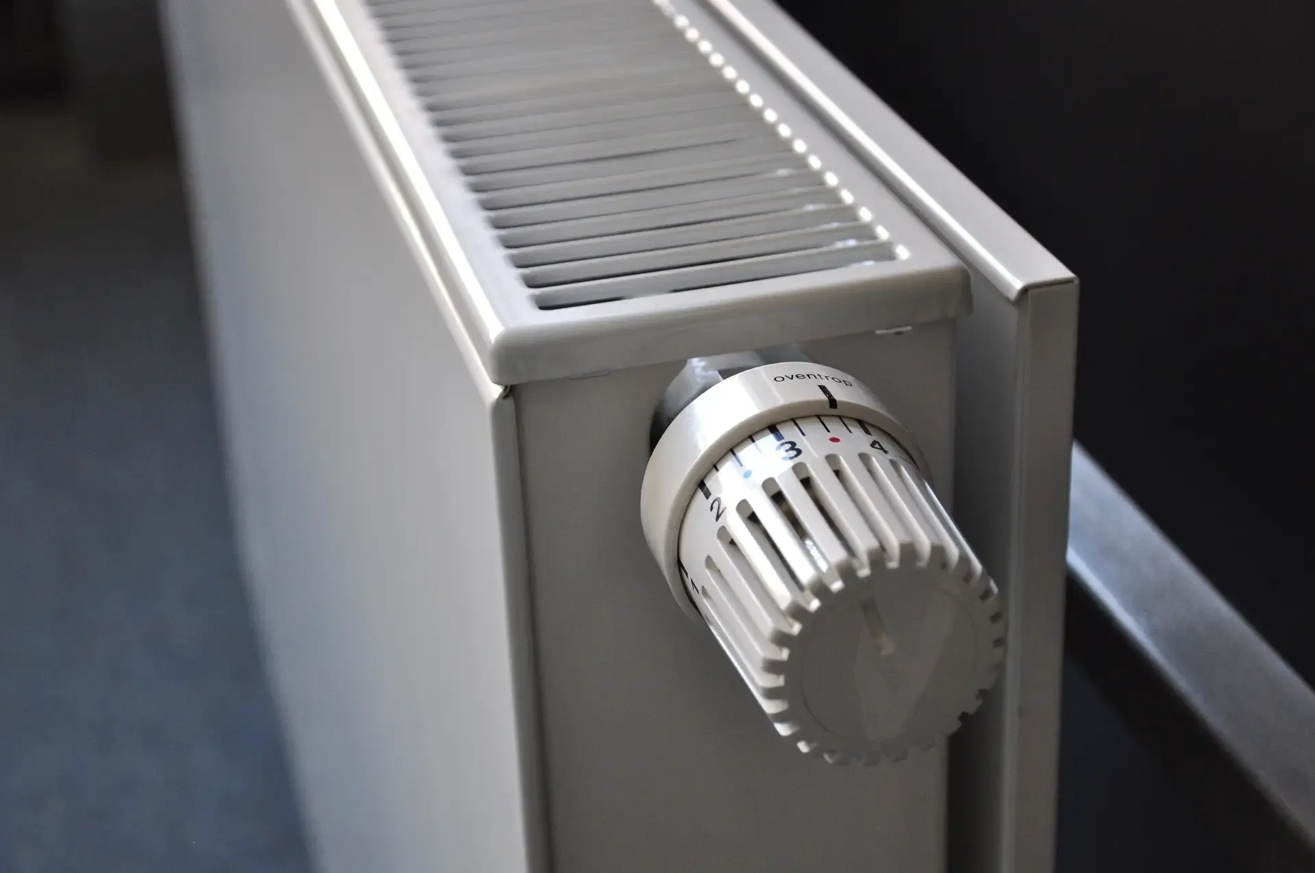 A homeowner checking a radiator with cold spots at the bottom indicating heating issues